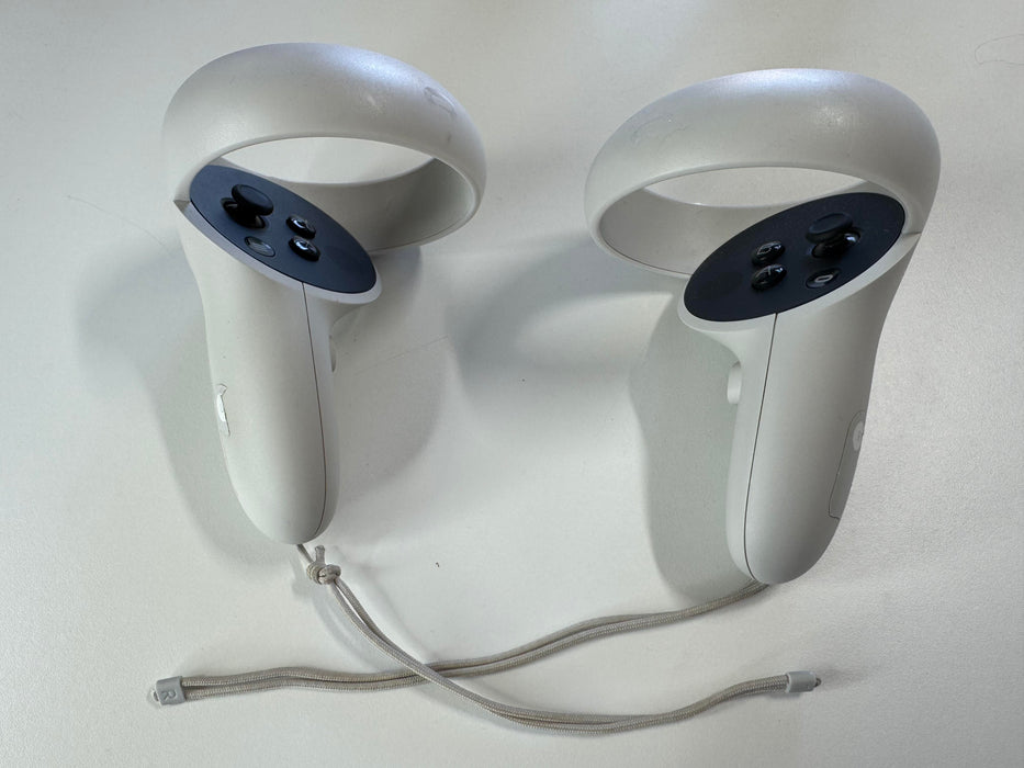 Two Meta Quest 2 controllers showing white tracking rings and ergonomic grips with thumbsticks and buttons for virtual reality gaming